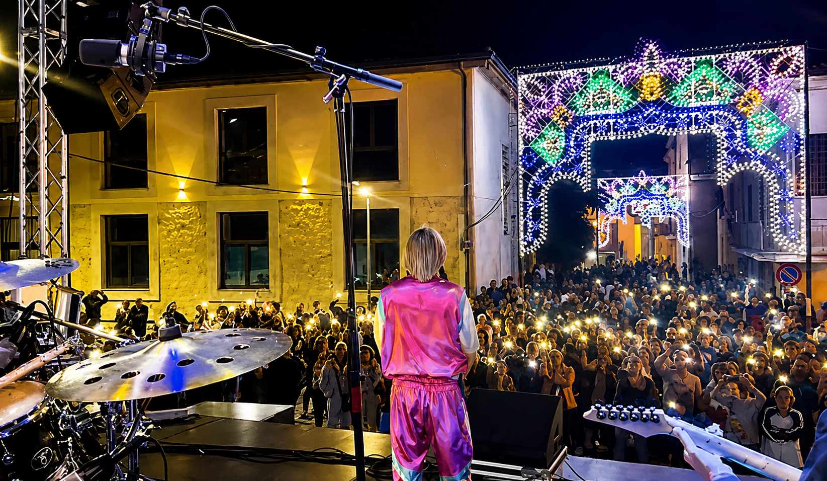 Nino Esposito di spalle sul palco davanti a una piazza illuminata a festa